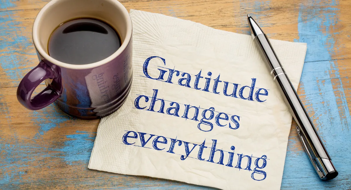 Blatt mit "Gratitude changes everything" (Dankbarkeit ändert alles" befindet sich unter einer Tasse Kaffee und einem Stift