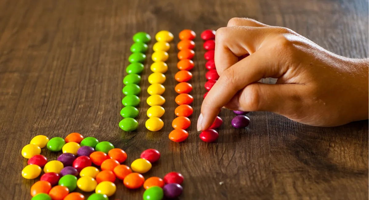 Burnout: Hand sortiert farbige Smarties nach Farben (rot, orange, gelb, grün)