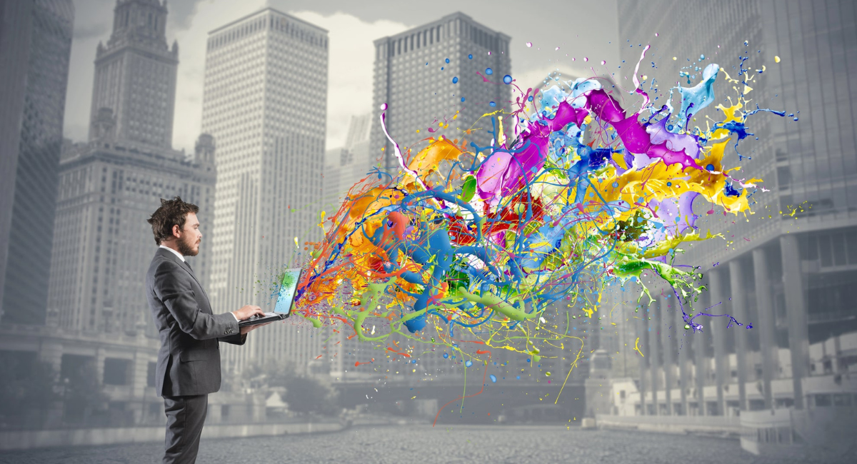 Mann im Anzug mit Laptop aus den diverser Farben sprudeln als Sinnbild für Kreativität